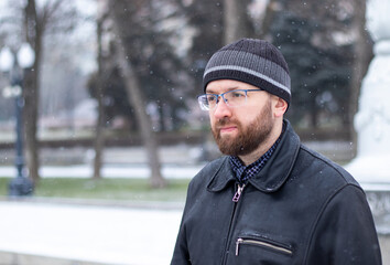 Portrait of adult serious man with beard and glasses in warm winter black clothes looking at side