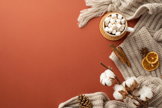 Top view photo of knitted scarf mug of hot drinking with marshmallow on rattan placemat dried orange slices pine cone anise cinnamon sticks cotton branch on isolated brown background with copyspace