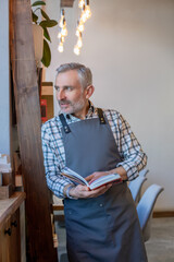 Bearded blue-eyed man in apron in the cafe premises
