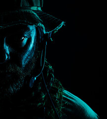 Special forces United States in Camouflage Uniforms studio shot. Wearing jungle hat, Shemagh scarf, painted face. Black background, bottom light colorized toned contour shor