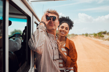 Road trip, travel and view with a couple using binoculars for sightseeing while outdoor on sand road during their summer vacation. Diversity, love and holiday with a man and woman traveling on a trip - Powered by Adobe