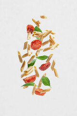 Flying pasta with tomatoes and basil on a gray background