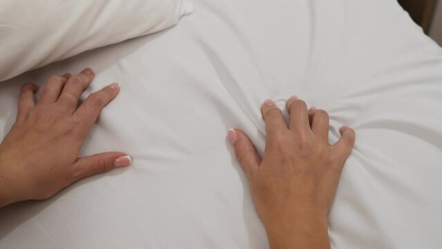 A woman's hand squeezes the sheet in bliss. Bright orgasm in a woman from sex and preliminary caresses