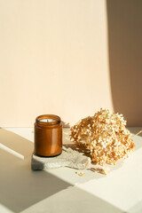 Scented handmade candles in a glass on a stone stand dry flowers on a beige background. Candles with wooden wick for home decor. Trendy colored background of the concept of nature and recreation.