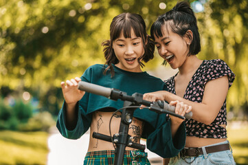 Two smiling girls with a scooter in the park