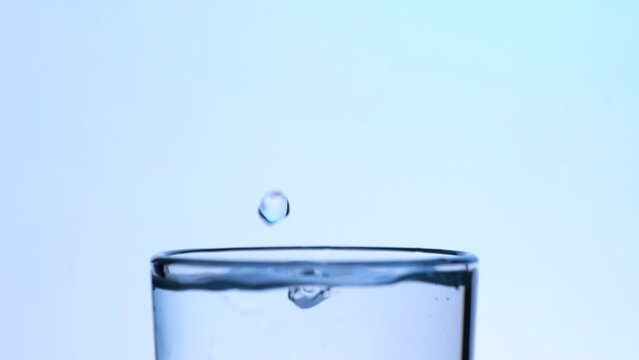 drops of water in a transparent glass on a blue background, slow motion