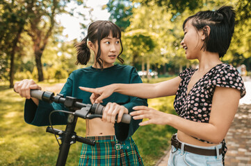 Two smiling girls with a scooter in the park