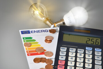 Energy efficiency rating table with illuminated light bulbs, calculator on gray background,...