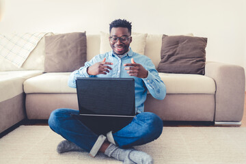 Smiling man with modern laptop. Shot of a young man using a laptop while relaxing in his living room, working from home.