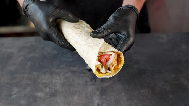 Presenting Shawerma d&ouml;ner kebab in tortilla wrap by the cook. Wearing gloves closeup. Vegetables and meat inside. Showing finished meal to client.