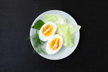 Halves of a hard boiled chicken egg with lettuce, dill and parsley on a plate on a dark background