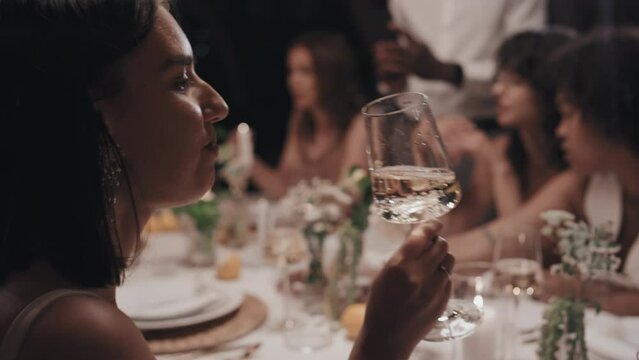 Selective Focus Of Young Caucasian Woman Sitting At Dining Table At Wedding Party In Restaurant Drinking Champagne And Talking To Friend