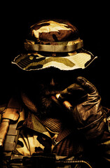 Brutal and serious commando soldier, army special forces veteran, in camouflage battle uniform, boonie hat, black paint on bearded face, combat knife in shoulder holder, smoking cigar, studio portrait