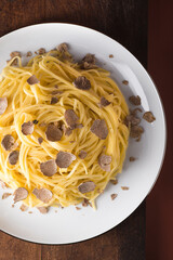 Season of white truffle.  Pasta Tajarin with  white truffle on antique  wooden board. Terracotta background, magical light in the style of the Chef's table, white plate, top view