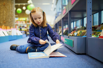 4 year old girl sitting on the floor in municipal library and reading a book