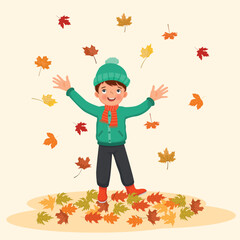 happy little boy playing outside with fallen leaves in autumn