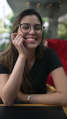 One happy young woman smiling at camera. Charming 20s girl wearing eyeglasses seated at coffee shop...