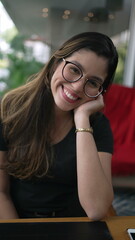 One happy young woman smiling at camera. Charming 20s girl wearing eyeglasses seated at coffee shop...