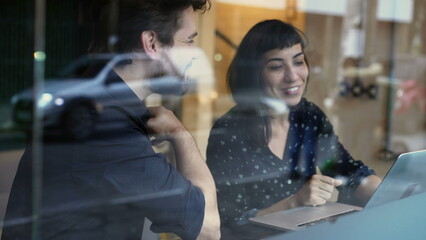 Young millennials discussing work or study seated by window in front of sidewalk urban street view reflection of cars and traffic passing by 2