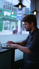 Fototapeta premium Young man typing on computer laptop seated at cafe workplace. Entrepreneur works remotely. Vertical Video