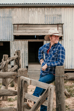 Farmer leans against stock yard fence.