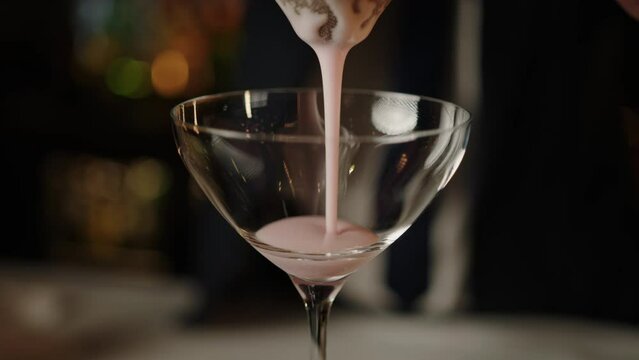 The bartender pours a frothy cocktail into a glass. Serving alcoholic cocktails at the bar. People's rest in the evening