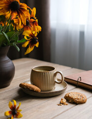 A cup of tea, a book and a vase of autumn flowers on a table by the window. Cozy autumn weekend