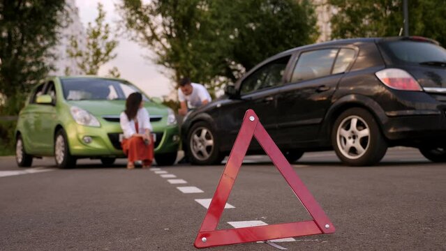 Red emergency stop triangle sign afore Destroyed car in car crash traffic accident on city road. Man driver looking on Smashed broken car in accident. Copy space.