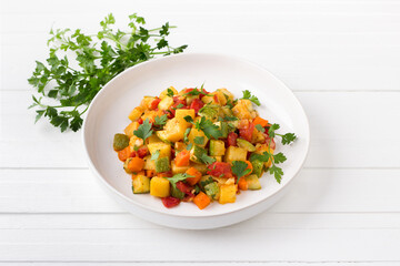 Vegetable stew with zucchini, carrots, potatoes and parsley on a white plate on a light gray background - 537262498
