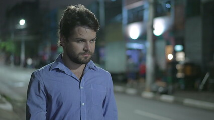 Fototapeta premium Pensive young man walking in city street at night. Thoughtful person walks in urban sidewalk in mental reflection in the evening