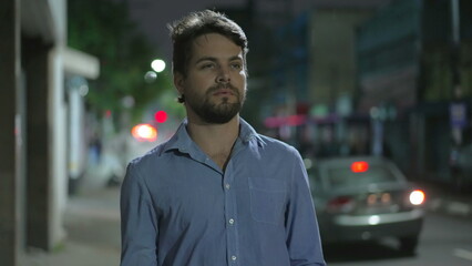 Pensive young man walking in city street at night. Thoughtful person walks in urban sidewalk in mental reflection in the evening