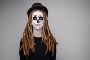 Portrait of a man in a skull suit. Traditional makeup for day of the dead mexico. Modern hipster with dreadlocks men's halloween makeup idea. carnival costume skeleton party. Gray mystery background 