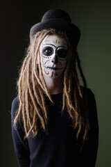 Portrait of a man in a skull suit. Traditional makeup for day of the dead mexico. Modern hipster with dreadlocks men's halloween makeup idea. carnival costume skeleton party. Dark mystery background 