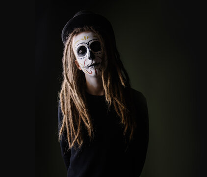 Portrait of a man in a skull suit. Traditional makeup for day of the dead mexico. Modern hipster with dreadlocks men's halloween makeup idea. carnival costume skeleton party. Dark mystery background 
