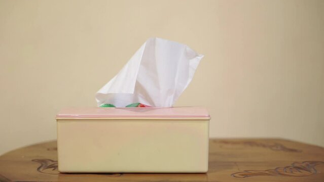 A hand takes tissue papers from the box on a table