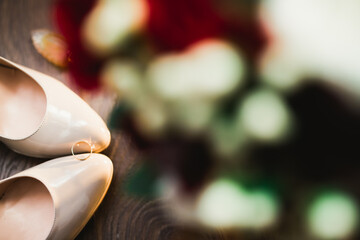 Pair of elegant and stylish bridal shoes with wedding rings and a bouquet of roses and other flowers