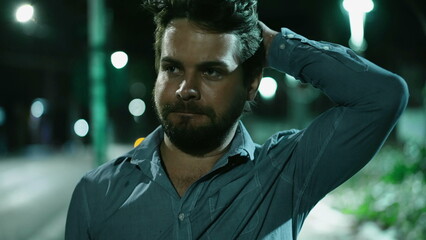 Serious young man walking at night in downtown city street. Thoughtful pensive person walks forward at night in urban sidewalk