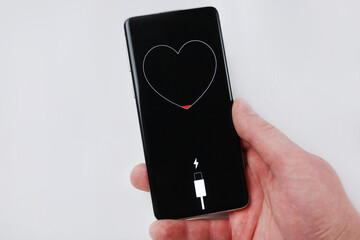 Smartphone in hand showing low battery in the form of a heart