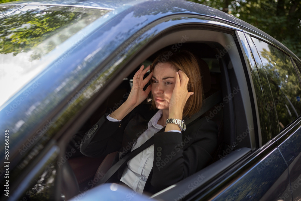 Wall mural young attractive businesswoman in suit driving and standing in a traffic jam. tired business lady si