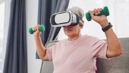 Asian senior woman wearing VR glasses and lifting dumbbells at home workout, virtual reality and metaverse concept.