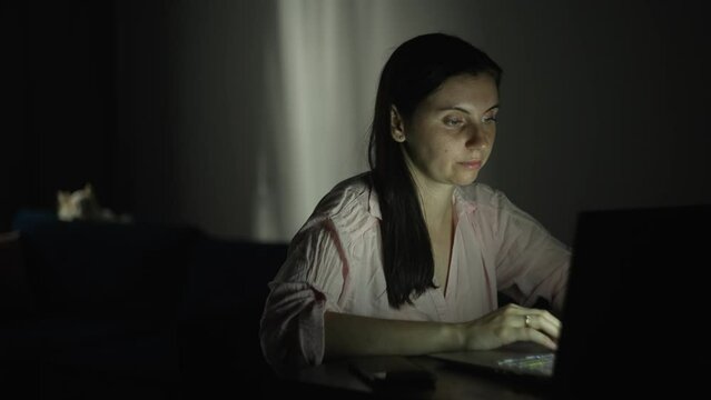 The girl works in the evening at home at the computer. A woman performs a task on a laptop. An apartment and a dog in the background. Remote work. High quality 4k footage