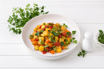 Vegetable stew with zucchini, carrots, potatoes and parsley on a white plate on a light gray background