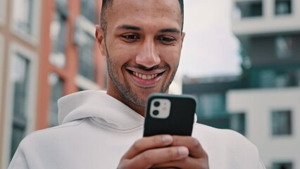 Joyful happy african latino man freelancer american guy stand on city street hold modern phone texting message make internet order search online media news distance communication use digital service - Powered by Adobe