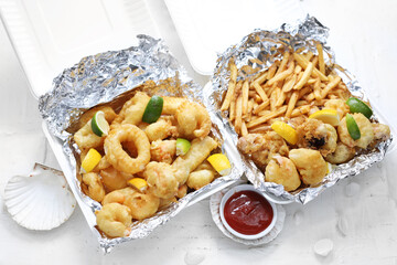 Deep fried calamari, squid rings and shrimps in tempura, with fries, in take-away carton boxes, on...