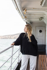Fototapeta na wymiar blonde woman in black sweater looking at sea from ferry boat crossing bosporus in istanbul.