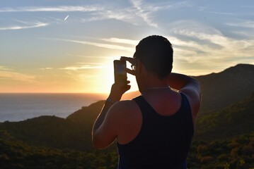 a man takes a photo of the sunset with a mobile phone