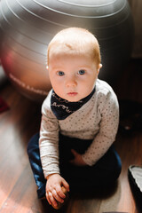 Toddler sitting on the floor in the game room with a fitness ball. Little boy child in nursery room. The baby playing in a children's playroom. Entertainment center.