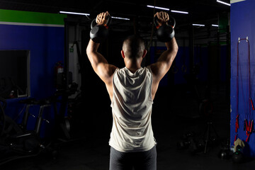 Fototapeta na wymiar latino man with sportswear, doing press with a pair of kettlebells in a gym