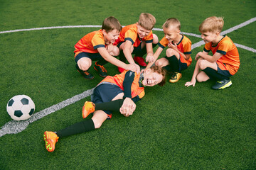 Naklejka premium Happy kids, beginner soccer players having rest after sports training at sports stadium, outdoors. Concept of sport, studying, art, education
