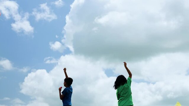 silhouette shot, back view of two preteen kids flying kite on blue clouded sky - concept of childhood freedom, siblings bonding and recreation